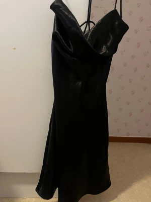 Svart satin klänning med smala band - Snygg svart klänning i satin med smala axelband och en draperad urringning samt öppen rygg. Klänningen har en elegant, figurnära passform och slutar strax ovanför knäna på mej (162cm). Perfekt för fest/speciella event! 💖 Aldrig använd 