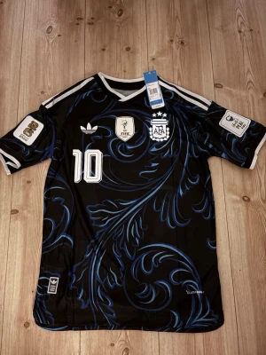 Argentina Messi matchtröja svart/blå - Snygg svart Argentina matchtröja med blått mönster och vita detaljer. Nummer 10 och Messi på ryggen, samt officiella FIFA och AFA-emblem på bröstet. Korta ärmar och sportig passform, perfekt för fotbollsfans. Skicka gärna pris förslag så kan vi lösa en bra affär. 