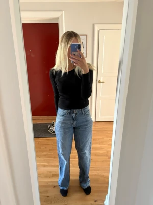 Blå raka jeans med hög midja - Säljer ett par ljusblå jeans med rak passform och hög midja. Jeansen har klassisk femficksdesign och är tillverkade i denim. Perfekta för en avslappnad och trendig look.