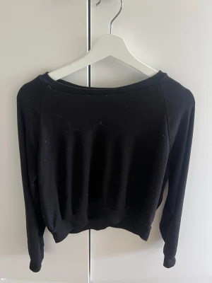 Svart croppad sweatshirt  - En enkel svart sweatshirt med rund halsringning och långa ärmar. Tröjan har en avslappnad passform och ribbade muddar vid ärmslut och nederkant. Perfekt att matcha med jeans eller mjukisbyxor för en chill look.