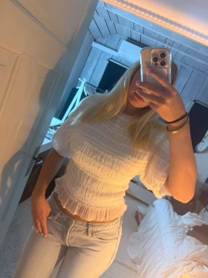 Vit blus - Säljer en söt vit blus med ribbad struktur och korta puffärmar. Toppen är croppad och har en lätt volangkant nedtill. Perfekt till jeans eller kjol för en fräsch look.