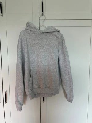 Ljusgrå basic hoodie med huva - En enkel och stilren ljusgrå hoodie med huva och magficka. Tillverkad i mjukt sweatshirtmaterial och har ribbade muddar vid ärmslut och nederkant. Perfekt för en avslappnad och bekväm look. Relaxed passform liknar Acne Studios hoodies.