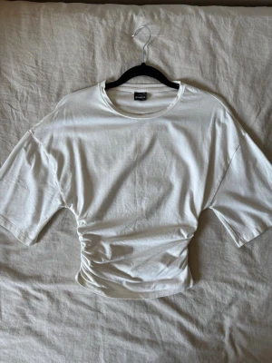 Vit topp med snörning i midjan - Säljer en vit topp med korta ärmar och snygg snörningsdetalj i midjan som ger en cool, croppad look. Tillverkad i mjukt bomullsmaterial och har en relaxed passform. Perfekt för dig som gillar stilrena plagg med en twist.