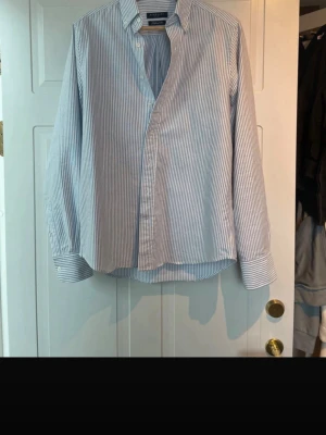 Randig skjorta från Berkeley  - Klassisk vit och blå randig skjorta från Berkeley i modellen Tailored Fit. Skjortan har långa ärmar, knappar framtill och en tidlös krage. Perfekt för dig som gillar en clean och stilren look.