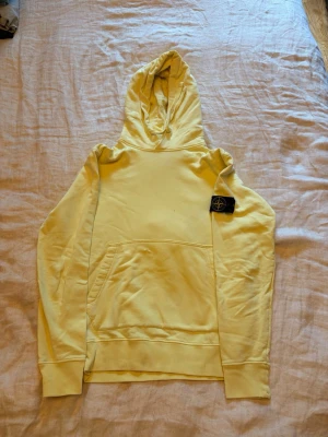 Stone Island Hoodie  - Stone Island hoodie – gul 💛  Snygg gul Stone Island hoodie med det klassiska Compass-märket på vänster ärm.  Clean och stilren modell i en riktigt snygg gul färg. Passar perfekt med jeans och sneakers.  Har ett litet hål på magen, vilket syns på bilderna. I övrigt bra begagnat skick.  Säljs därför till ett lägre pris.
