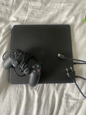 PlayStation 4 med en handkontroll  - Säljer en svart PlayStation 4 i modell 2216 Afrån Sony med en  svarthandkontroll och tillhörande strömkabel.  Konsolen har en stilren, matt finish och den klassiska PlayStation-loggan på ovansidan. Perfekt för gamingkvällar med vänner. Helt oanvänd 