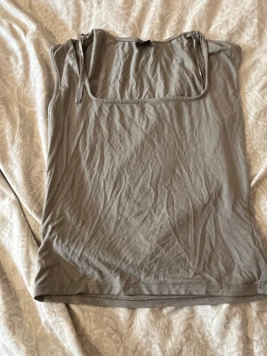 Beige linnetopp från Gina Tricot - Säljer en enkel och stilren beige linnetopp från Gina Tricot. Toppen har smala axelband med knyt på ena sidan och är tillverkad i mjuk bomull. Perfekt att matcha med jeans eller kjol för en avslappnad look.