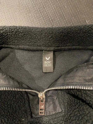Svart fleecejacka från SOC - Mysig svart fleecejacka från SOC med hög krage och dragkedja framtill. Tillverkad i mjukt fleecematerial som håller dig varm. Perfekt för kyliga dagar och enkel att matcha med andra plagg.