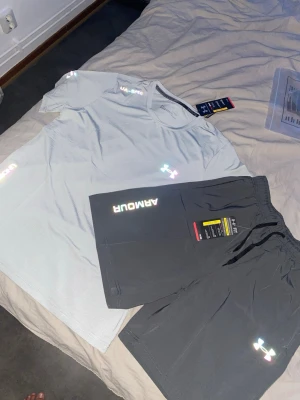 Svarta träningsshorts från Under Armour - Snygga svarta träningsshorts från Under Armour med elastisk midja och logga på benet. Shortsen har en loose passform och är tillverkade i ett lätt syntetmaterial som andas, perfekt för träning och sportaktiviteter.