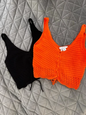 Stickade linnetoppar från Amisu - Två stickade linnetoppar från Amisu i färgerna svart och orange. Båda topparna har snörning framtill, v-ringad hals och är ärmlösa. Perfekta för sommaren och ger en trendig och avslappnad look.