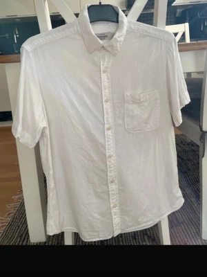Vit linneskjorta från Dressmann - Klassisk vit skjorta från Dressmann i linnemix. Skjortan har korta ärmar, bröstficka och knappar framtill. Perfekt för varma dagar och enkel att styla till olika outfits.