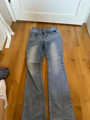 Blå bootcut jeans med slitningar - Ett par ljusblå bootcut jeans med snygga slitningar framtill och klassiska fem fickor. Jeansen har en hög midja och är tillverkade i denim med lätt stretch. Perfekta för en avslappnad och trendig look.