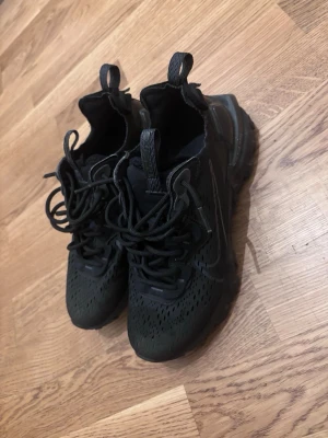 Svarta sneakers nike  - Säljer ett par svarta nike sneakers, vågig sula och ventilerande meshdetaljer. Skorna har snörning, dragflikar både fram och bak samt en diskret logga på sidan. Perfekta för dig som gillar sportig och modern stil.