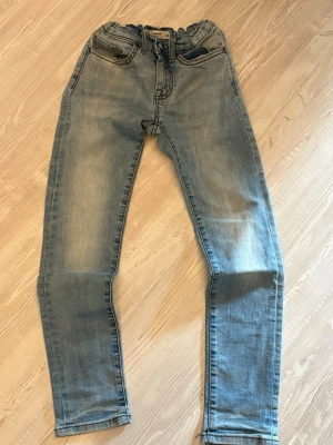 Ljusblå raka jeans med resårmidja - Säljer ett par ljusblå jeans med raka ben och resår i midjan. Jeansen har klassiska fem fickor och subtila slitningar framtill för en avslappnad look. Perfekta till vardags och lätta att matcha med olika stilar.