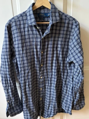 Blå rutig skjorta från Polo Ralph Lauren - Snygg blå rutig skjorta från Polo Ralph Lauren med klassisk krage och långa ärmar. Skjortan har knäppning framtill och är tillverkad i mjuk bomull. Perfekt för en avslappnad men stilren look. 