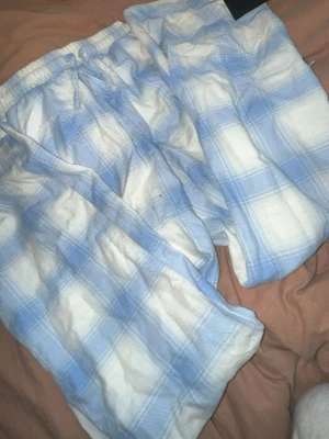 Blåvitrutiga pyjamasbyxor - Mysiga pyjamasbyxor i blåvitt rutigt mönster. Byxorna har resår i midjan med dragsko för skön passform och är gjorda i ett mjukt, tunt tyg som passar perfekt för att chilla hemma. Klassisk och avslappnad stil.