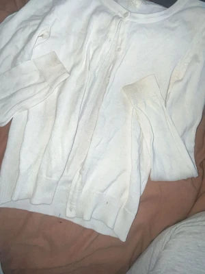 Vit kofta från H&M BASIC XS - Klassisk vit kofta från H&M BASIC i storlek XS. Koftan har rund halsringning, långa ärmar och knäppning framtill med små vita knappar. Ribbstickade muddar vid ärmslut och nederkant ger en enkel och clean look.