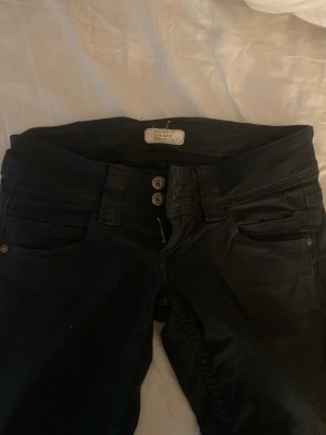 Lågmidjade jeans - Svarta lågmidjade jeans med dubbla knappar i midjan och klassiska fem fickor. Mjukt och bekvämt material och dom sitter inte tajt på mig. Köpte dom för ett tag sen på plick så dom var sydda så dom skulle vara bootcut när jag köpte dom, jeansen är även sydda så dom ska vara längre. Ser inte någonstans vart storleken är men dom är 38cm rakt över midjan och 78cm i benlängd så skulle säga XS-S. Skriv för bilder eller annat pris! ☺️