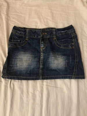 Jeanskjol, storlek 38 - Snygg blå jeanskjol från ONLY i klassisk denim med slitningar framtill och kontrastsömmar. Modellen är kort och har fickor både fram och bak. Perfekt att matcha med en t-shirt eller hoodie för en avslappnad look. 