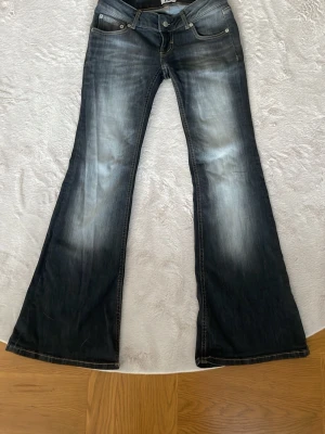 Mörkblå bootcut jeans med slitningar - Säljer ett par svarta bootcut jeans med snygga slitningar och ljusa tvättade partier framtill och baktill. Jeansen har klassisk femficksmodell, låg midja och vida ben. Perfekta för dig som gillar retrostil och vill ha ett par jeans som sticker ut. De är i storlek M men är ganska så korta för mig som är 164.