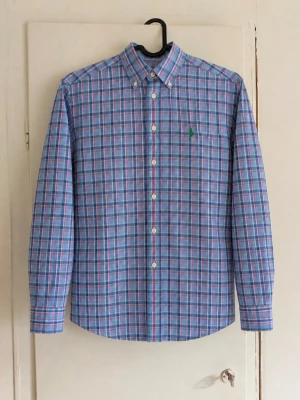 Ralph Lauren skjorta - Klassisk långärmad skjorta i blått med rutigt mönster och grön broderad logga på bröstet. Button-down-krage och tidlös passform. Fin både till vardags och lite mer uppklätt. Skick: Fint begagnat skick , den har inga defekter! Skriv gärna vid frågor eller för fler bilder 💌