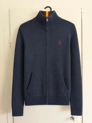 Polo Ralph Lauren stickad zip-tröja marinblå - Klassisk stickad zip-tröja/kofta från Polo Ralph Lauren i marinblått 💙 Hel dragkedja framtill, två framfickor och röd broderad Polo-logga på bröstet. Ribbad hög krage med en snygg röd/gul detalj baktill som sticker ut lite extra. Storlek: L (14-16) Färg: Marinblå Skick: Fint begagnat skick men den är lite färg blekt och har en fläck! Modell: Stickad full zip med hög krage Väldigt snygg till jeans eller chinos och perfekt som lager under höst/vår 🍂