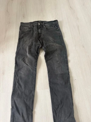 Svarta jeans från Replay, raka ben - Säljer ett par svarta jeans från Replay med raka ben och klassisk femficksmodell. Jeansen har diskreta slitningar och är tillverkade i bomull med lite stretch för extra komfort. Perfekta för en avslappnad och stilren look.