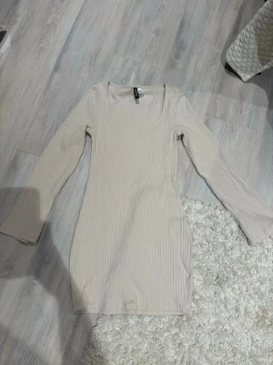 Beige ribbad långärmad klänning - Snygg beige ribbad klänning med lång ärm och fyrkantig urringning. Klänningen är kroppsnära och har en mjuk, stretchig känsla. Perfekt för dig som gillar en enkel men trendig look.