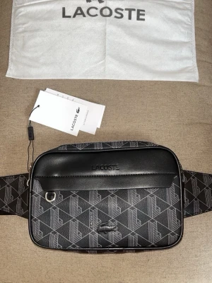 🖤 LACOSTE Crossbody-väska  - Snygg Lacoste axel-/crossbodyväska i svart med det klassiska Lacoste-mönstret och krokodil-loggan. Perfekt för dig som vill bära mobil, plånbok, nycklar och andra småsaker med stil.