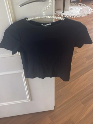 Svart ribbad croppad topp - En svart, croppad topp med ribbad struktur och korta ärmar. Perfekt till höga jeans eller kjol. Enkel och stilren design som passar till det mesta.