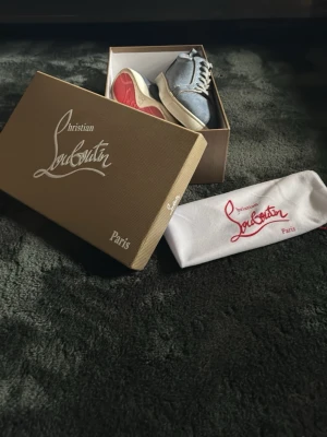 Blåa sneakers från Christian Louboutin - Snygga blåa sneakers i mocka från Christian Louboutin med klassisk röd sula och vita kanter. Skorna har rund tå, matchande blå skosnören och diskret branding på sulan. Perfekta för dig som vill sticka ut med exklusiv stil. Bara använda ett fåtal gånger.