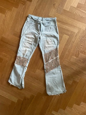 Ljusblå jeans med spetsdetaljer - Unika ljusblå jeans med vida ben och råa kanter. Båda benen har stora insydda partier av beige spets som ger en cool kontrast och trendig look. Perfekta för dig som vill sticka ut och gillar statement-plagg. Materialet är denim med inslag av spets.