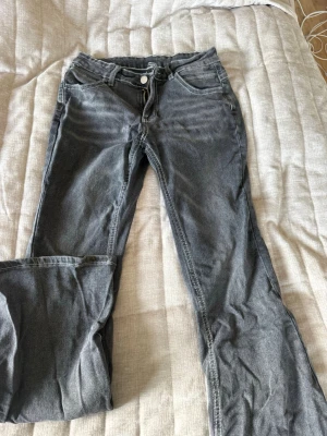 Grå bootcut jeans med vita sömmar - Säljer ett par grå jeans med bootcut-modell och tydliga vita kontrastsömmar. Klassisk femficksdesign och bälteshällor. Jeansen har dragkedja och knapp framtill och är tillverkade i denim med lite stretch.