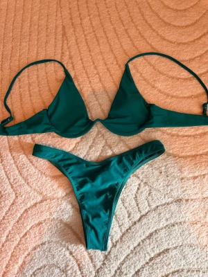 Mörkgrön bikini med triangeltopp - Snygg mörkgrön bikini med enkel triangeltopp och matchande trosa med hög skärning. Båda delarna har tunna axelband och är tillverkade i ett mjukt, stretchigt material som sitter skönt på kroppen. Perfekt för lata dagar på stranden eller poolen. Helt oanvänd 