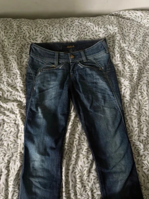 Blå jeans från Killah  - Säljer ett par blå jeans från Killah med snygga slitningar och tvättade detaljer. Klassisk femficksmodell med raka ben och normal midja. Jeansen har kontrastsömmar och metallknapp i midjan. Perfekta för en avslappnad och trendig look.
