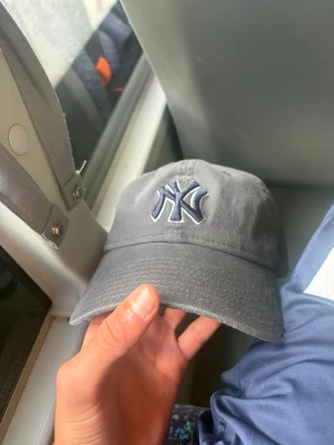 Grå New York Yankees keps - Snygg grå keps från New Era med New York Yankees-logga broderad framtill i mörkblått och vitt. Klassisk böjd skärm och justerbar passform bak. Tillverkad i bomullstyg som känns mjukt och bekvämt. Perfekt för dig som vill ha en stilren och sportig look.