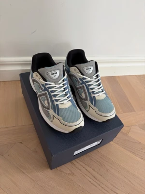 B30 sneakers blå och beige - Ett par snygga B30, färgen ljus blå med vita och beige detaljer. Skorna kommer med box samt tillbehör som ett par extra sko snören och en påse till skorna, Är i ny skick. Säljer eftersom de var för små.