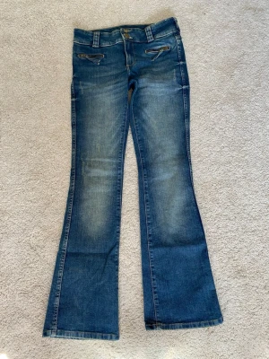 Blå bootcut jeans - Snygga blå bootcut jeans med dragkedjor på fickorna framtill och klassiska bakfickor. Jeansen har en lätt tvättad look och utsvängda ben. 