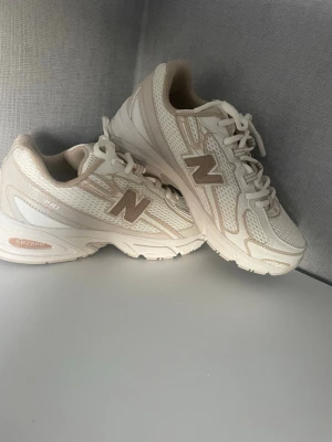 New balance 740 - Snygga sneakers från New Balance i beige och vitt med mesh- och syntetdetaljer. Klassisk modell med lågt skaft, snörning och den ikoniska N-loggan på sidan. Perfekta för en clean och sportig stil.