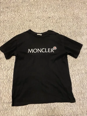 Svart Moncler t-shirt med logga - Snygg svart t-shirt från Moncler med stor vit logga och ikonisk patch på bröstet. Klassisk passform och rund halsringning. Perfekt till jeans eller shorts för en clean och stilren look.