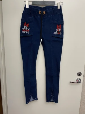 Blå jeans med Minnie Mouse, stl XS - Mörkblå jeans med broderade Minnie Mouse-motiv och texten 'BFFS' på fickorna. Byxorna har resårmidja med snörning, stora fickor framtill och dekorativa pärlor vid bensluten. Materialet ser ut att vara stretchigt och bekvämt, perfekt för en avslappnad look. Stl XS-SHämtas i Stockholm (Sundbyberg) eller skickas med posten, köparen står för frakten.   Kika på alla mina annonser. Köp mer med samfraktpris och spara på fraktkostnaden.