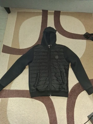 Philipp plein cardigan  - Säljer en svart cardigan med huva och dragkedja framtill. Jackan har quiltad front, släta ärmar och två fickor med dragkedja. Perfekt för dig som vill ha en stilren och sportig look. Den har inga innefickor men vill man så går det att sy så det finns det. Har inte fast pris, kom o förhandla! Står strl L men sitter som M/lite större S
