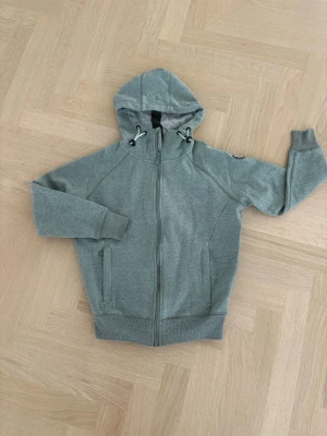 Hoodie från Pelle P, XS - Snygg grön hoodie från Pelle P i storlek XS. Hoodien har dragkedja framtill, två fickor och justerbar huva med snören. Insidan är mjuk och skön, perfekt för chill dagar. Klassisk design med ribbade muddar och diskret logga på ärmen. Som ny, knappt använd.