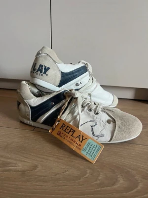Vita och blå Replay sneakers strlk 45 - Snygga sneakers från Replay i vitt och marinblått med detaljer i mocka och läder. Skorna har snörning, metallnitar och en broderad 'R' på sidan. 