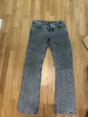 Grå tvättade raka jeans - Säljer ett par grå tvättade jeans med raka ben och hög midja. Jeansen har knappgylf och klassiska fem fickor. Materialet är denim med en snygg tvättad look som ger en retrovibe. Perfekta för dig som gillar en avslappnad och trendig stil. Använda 5 gånger snygga till ett par lavins eller Valentina skor 
