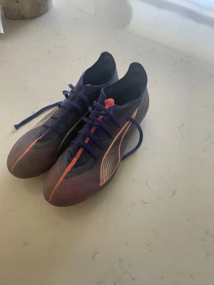 Lila och orangea fotbollsskor - Säljer ett par snygga fotbollsskor i lila med orangea detaljer och snörning. Skorna har en smal siluett och är designade för bra grepp på planen. Perfekta för dig som vill sticka ut på matchen!