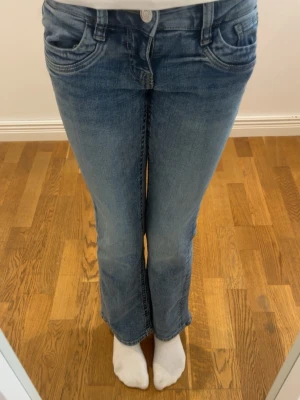 Blå bootcut jeans med utsvängda ben - Säljer ett par klassiska blå bootcut jeans med utsvängda ben och femficksmodell. Jeansen har normal passform och är tillverkade i mjuk bomull med snygga slitningar framtill. Perfekta för dig som gillar retrovibbar och vill ha ett par jeans som sticker ut.