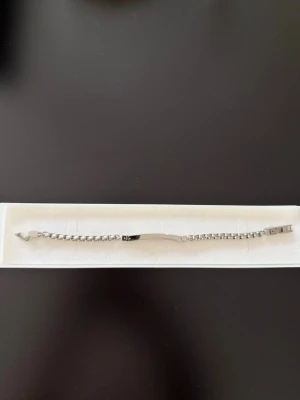 Silverfärgat kedjearmband i metall - Snyggt och stilrent armband i silverfärgad metall med en platt bricka i mitten och klassisk kedjedesign. Perfekt för dig som gillar minimalistiska accessoarer och vill ha något som passar till många olika outfits. Låset är enkelt och smidigt. Armbandet är väldigt stort och kan bli klipp och knäppt för att justera till just din arm, darför sänker jag priset rejält. 