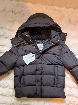 Moncler Vezere Jacka - Snygg svart dunjacka från Moncler med avtagbar huva, stora fickor med dragkedja och klassisk Moncler-logga på ärmen. Jackan har en puffig design och stängs med både dragkedja och knappar. Perfekt för kalla vinterdagar.