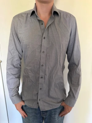 Grå under skjorta från ETERNA - Snygg grå skjorta med diskret mönster och klassisk krage. Skjortan har långa ärmar och knäppning framtill. Slim fit, storlek 40 (L). Knappt använd. Hör av dig om du har några frågor eller vill ha fler bilder. Pris kan diskuteras! 
